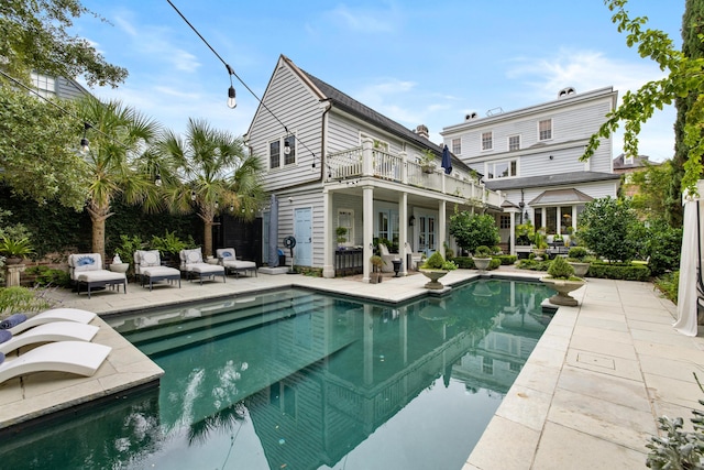 rear view of property featuring a patio, a balcony, a swimming pool with hot tub, and an outdoor living space