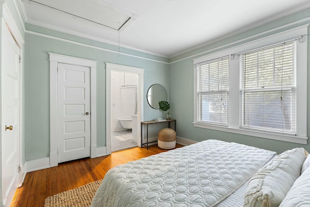 bedroom featuring wood finished floors, baseboards, attic access, ensuite bathroom, and crown molding