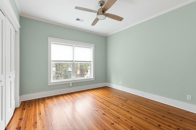 unfurnished bedroom featuring visible vents, baseboards, hardwood / wood-style floors, ornamental molding, and a closet