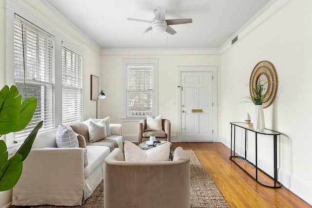 living room with ceiling fan, visible vents, light wood-style flooring, and crown molding