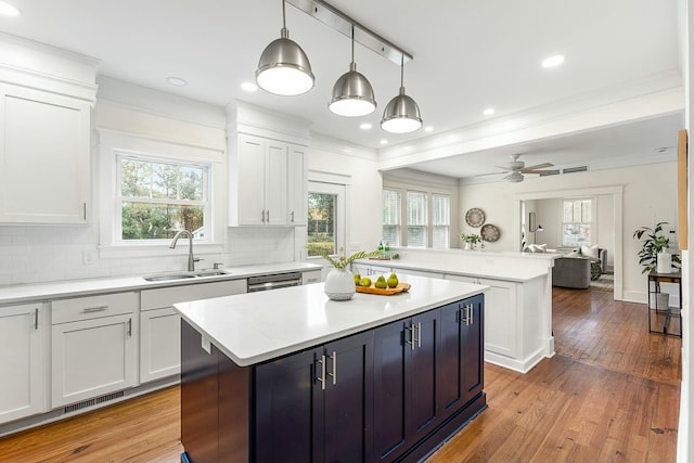 kitchen featuring light wood-style flooring, a sink, a peninsula, white cabinets, and light countertops