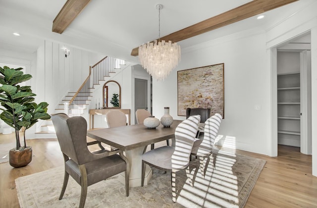 dining room with light wood finished floors, a notable chandelier, beam ceiling, and stairs