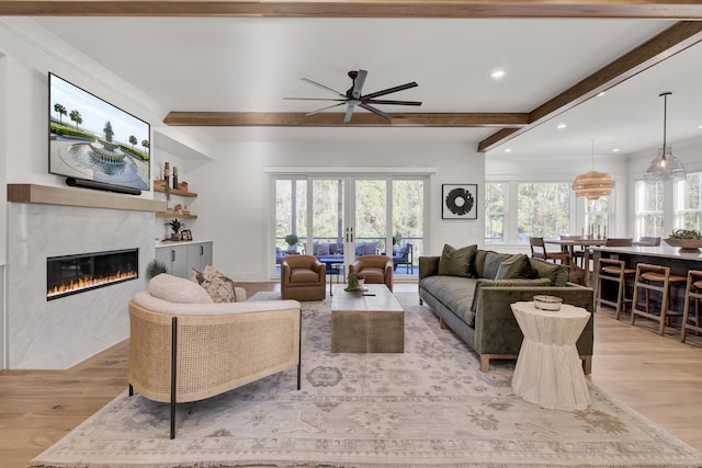 living area with ceiling fan, light wood-style floors, beam ceiling, and a glass covered fireplace