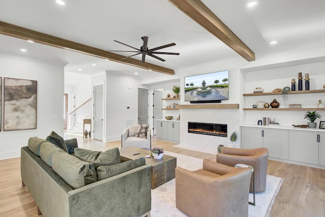 living area featuring beamed ceiling, a fireplace, light wood-style floors, and a ceiling fan