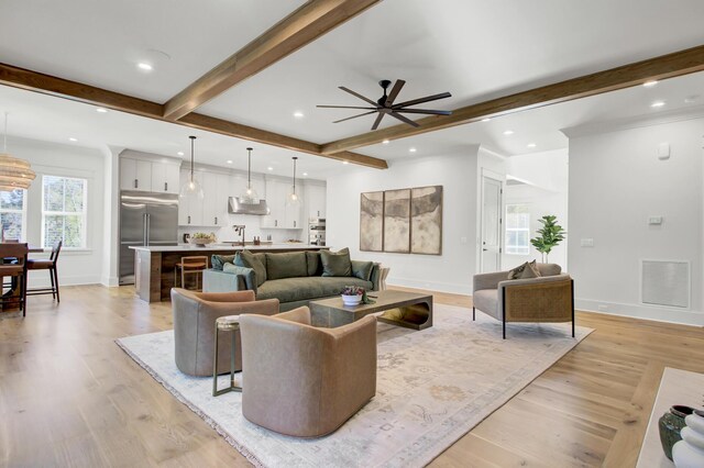 living room featuring baseboards, visible vents, light wood-type flooring, and beam ceiling