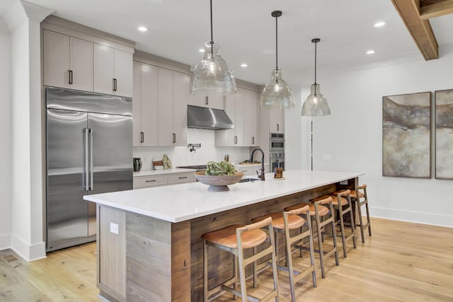kitchen with light countertops, stainless steel appliances, under cabinet range hood, and light wood-type flooring