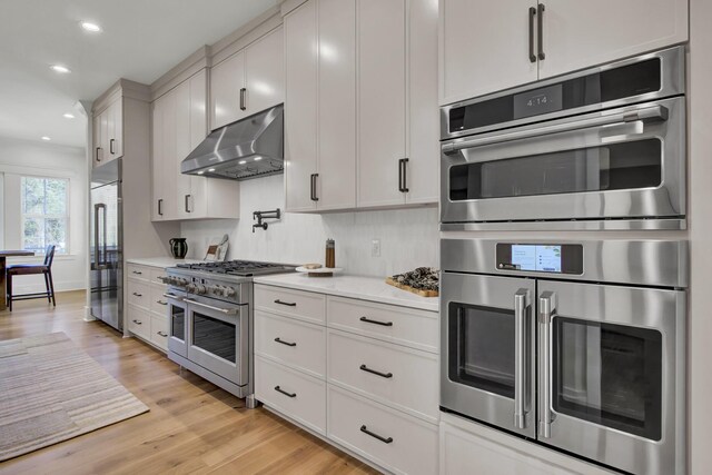 kitchen with light countertops, recessed lighting, light wood-type flooring, under cabinet range hood, and high end appliances