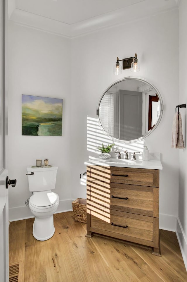 half bath with crown molding, toilet, vanity, and wood finished floors