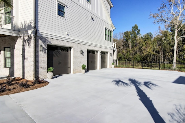 view of home's exterior featuring fence, board and batten siding, driveway, brick siding, and a garage