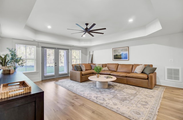 living area with french doors, a raised ceiling, light wood-style flooring, visible vents, and ceiling fan