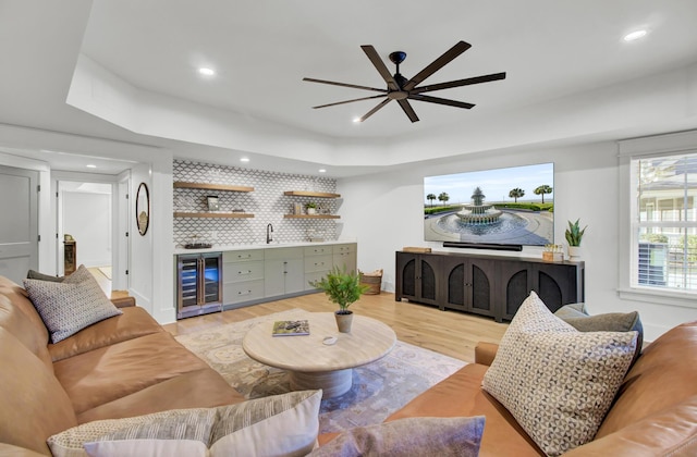 living room featuring a tray ceiling, beverage cooler, indoor wet bar, and a ceiling fan