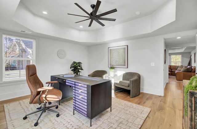 office space with baseboards, light wood-style flooring, ceiling fan, and a raised ceiling