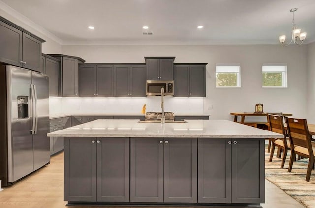 kitchen featuring ornamental molding, appliances with stainless steel finishes, light stone counters, and an island with sink