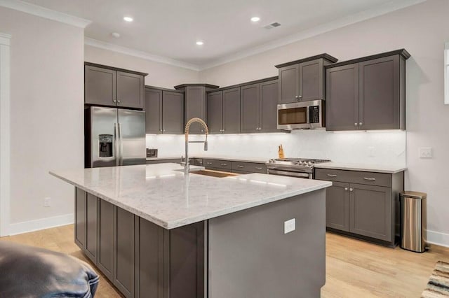 kitchen featuring stainless steel appliances, a center island with sink, sink, ornamental molding, and light hardwood / wood-style flooring