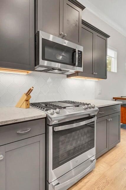 kitchen featuring tasteful backsplash, light stone counters, ornamental molding, stainless steel appliances, and light wood-type flooring