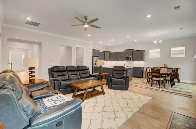 living room featuring light wood-type flooring, sink, crown molding, and ceiling fan with notable chandelier