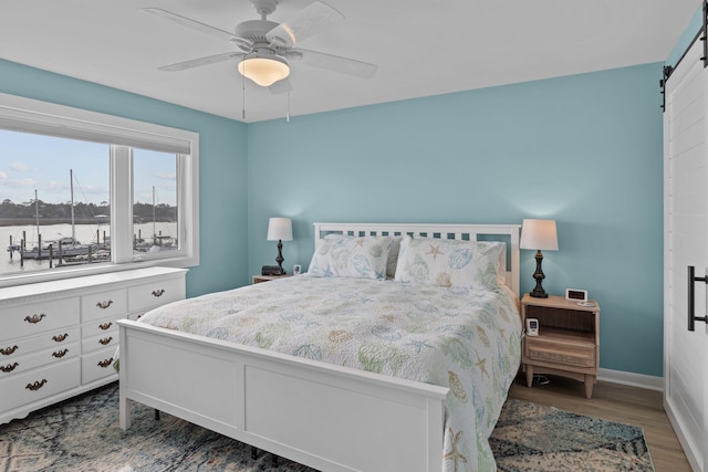 bedroom with hardwood / wood-style flooring, a barn door, ceiling fan, and a water view