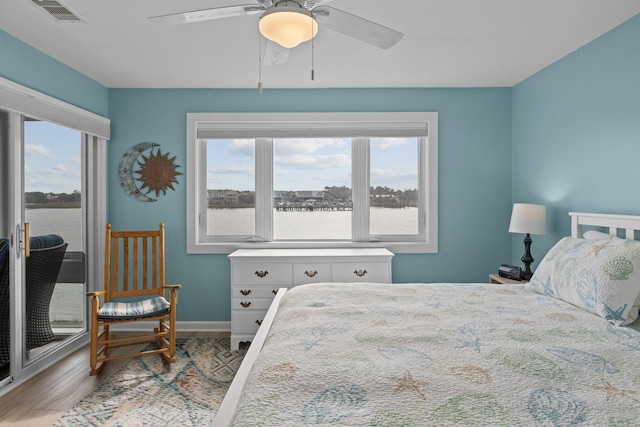 bedroom featuring light wood-type flooring, ceiling fan, and a water view