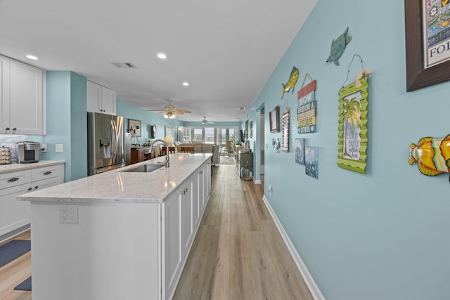 kitchen with stainless steel fridge with ice dispenser, sink, white cabinets, and a center island with sink