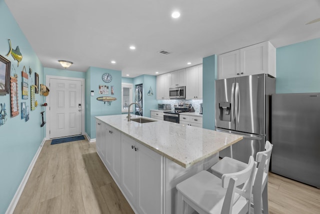 kitchen with sink, a kitchen island with sink, stainless steel appliances, light stone counters, and white cabinets