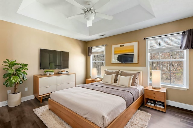 bedroom featuring a tray ceiling, visible vents, dark wood finished floors, and baseboards