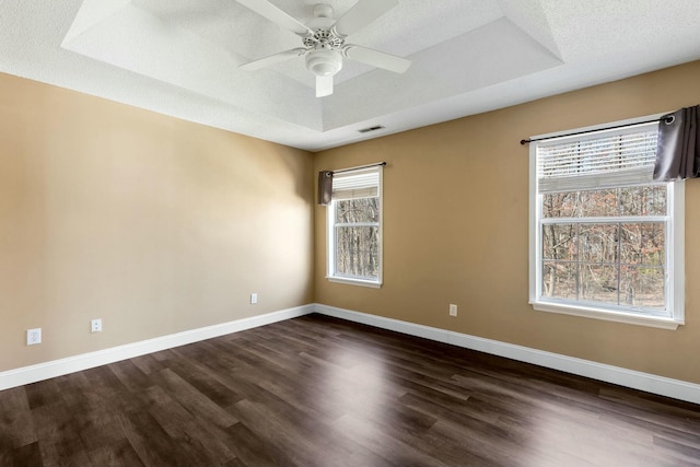 spare room with a tray ceiling, visible vents, dark wood finished floors, and baseboards