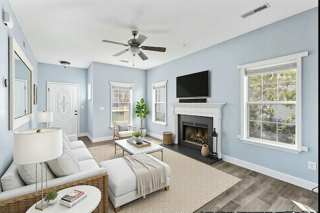 living room featuring baseboards, visible vents, a ceiling fan, a fireplace with raised hearth, and wood finished floors