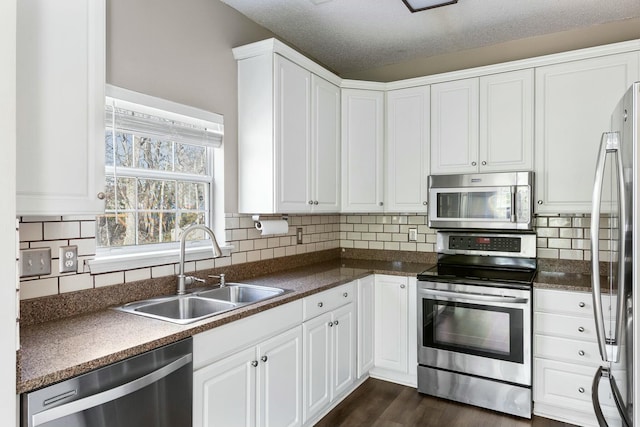 kitchen with dark wood finished floors, dark countertops, appliances with stainless steel finishes, white cabinets, and a sink