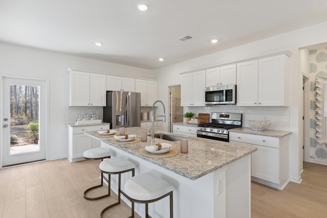 kitchen featuring visible vents, a kitchen island with sink, a sink, stainless steel appliances, and light wood finished floors