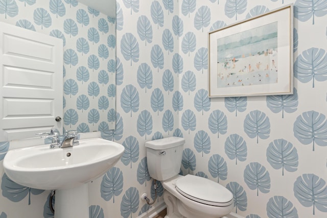 half bathroom featuring wallpapered walls, toilet, and a sink