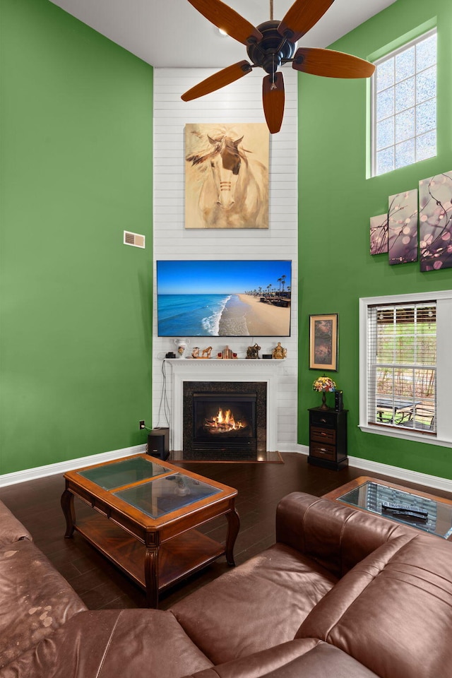 living area featuring a fireplace, visible vents, a high ceiling, wood finished floors, and baseboards