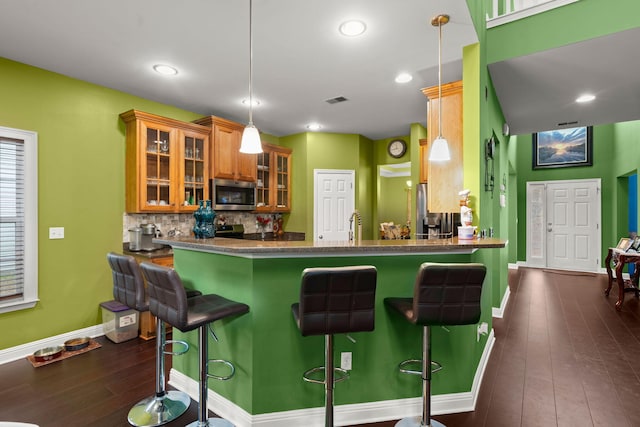 kitchen featuring dark wood-style floors, brown cabinets, tasteful backsplash, stainless steel microwave, and a kitchen breakfast bar