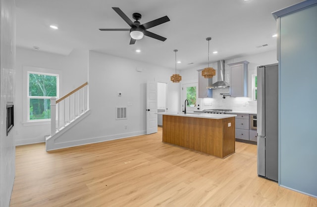 501 Joseph St, Charleston, SC 29412 - kitchen with wall chimney exhaust hood, light wood-style floors, light countertops, freestanding refrigerator, and an island with sink