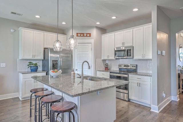 kitchen with wood finished floors, visible vents, a sink, stainless steel appliances, and a kitchen breakfast bar