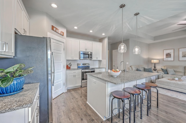 kitchen featuring open floor plan, a breakfast bar area, light wood-style flooring, appliances with stainless steel finishes, and white cabinetry