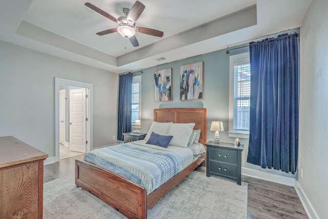 bedroom with a tray ceiling, baseboards, visible vents, and wood finished floors