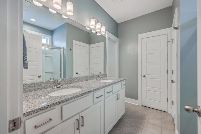 bathroom with a sink, a shower with shower door, double vanity, and tile patterned flooring