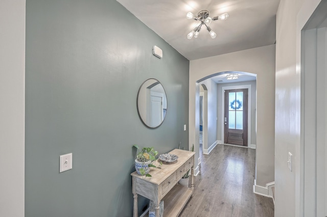 entryway with wood finished floors, arched walkways, and baseboards