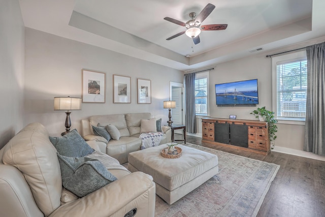 living room featuring a tray ceiling, plenty of natural light, hardwood / wood-style floors, and a ceiling fan