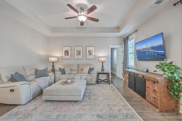 living area featuring a tray ceiling, visible vents, wood finished floors, and ceiling fan