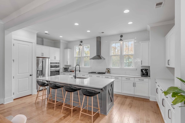 kitchen featuring wall chimney exhaust hood, light hardwood / wood-style floors, a kitchen bar, white cabinets, and appliances with stainless steel finishes