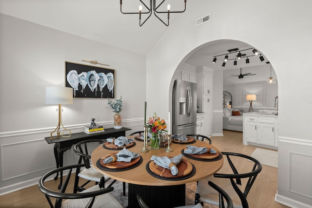 dining room with visible vents, light wood finished floors, ceiling fan with notable chandelier, arched walkways, and a decorative wall