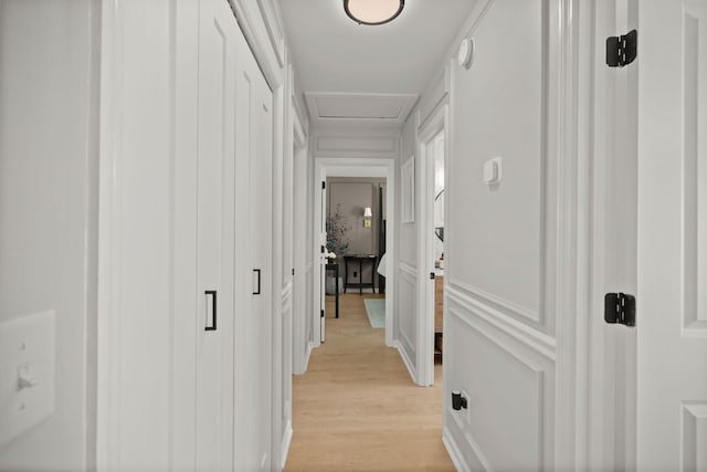 hall with attic access, a decorative wall, and light wood finished floors