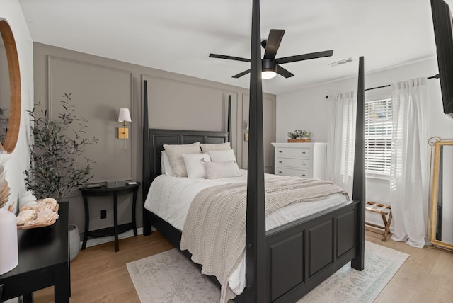 bedroom with a ceiling fan, a decorative wall, light wood-style floors, and visible vents