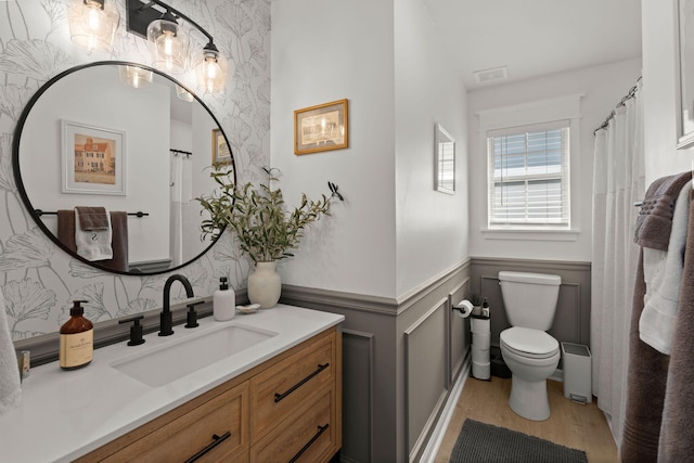 full bathroom with wallpapered walls, toilet, wainscoting, wood finished floors, and vanity