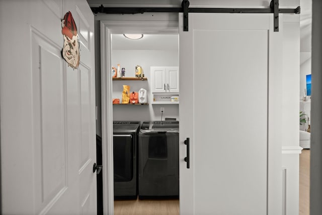 washroom with laundry area, light wood-style flooring, a barn door, and washing machine and clothes dryer