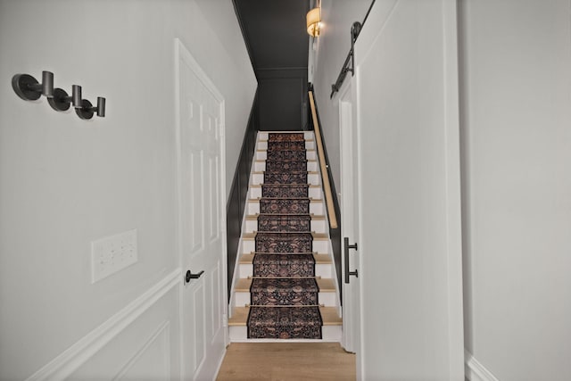 stairway featuring a barn door and wood finished floors