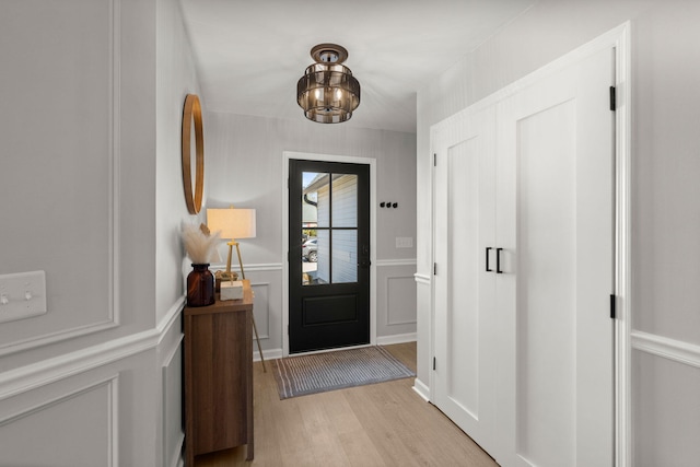 foyer entrance featuring a chandelier, a decorative wall, wainscoting, and light wood-style floors