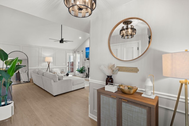 living room featuring vaulted ceiling, ceiling fan with notable chandelier, recessed lighting, wood finished floors, and a decorative wall