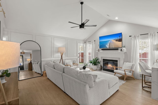 living room with light wood finished floors, a decorative wall, a fireplace with flush hearth, and a ceiling fan